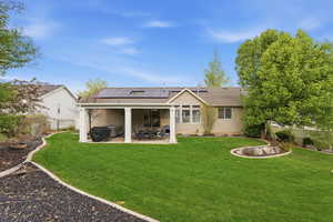 Rear view of property featuring solar panels, roof with shingles, a fenced backyard, and a patio