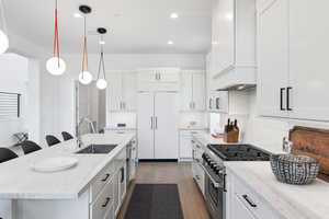 Kitchen featuring a kitchen breakfast bar, stainless steel gas stove, light stone countertops, dark wood finished floors, and a kitchen island with sink