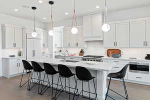 Kitchen featuring a breakfast bar, dark wood finished floors, hanging light fixtures, and a center island with sink