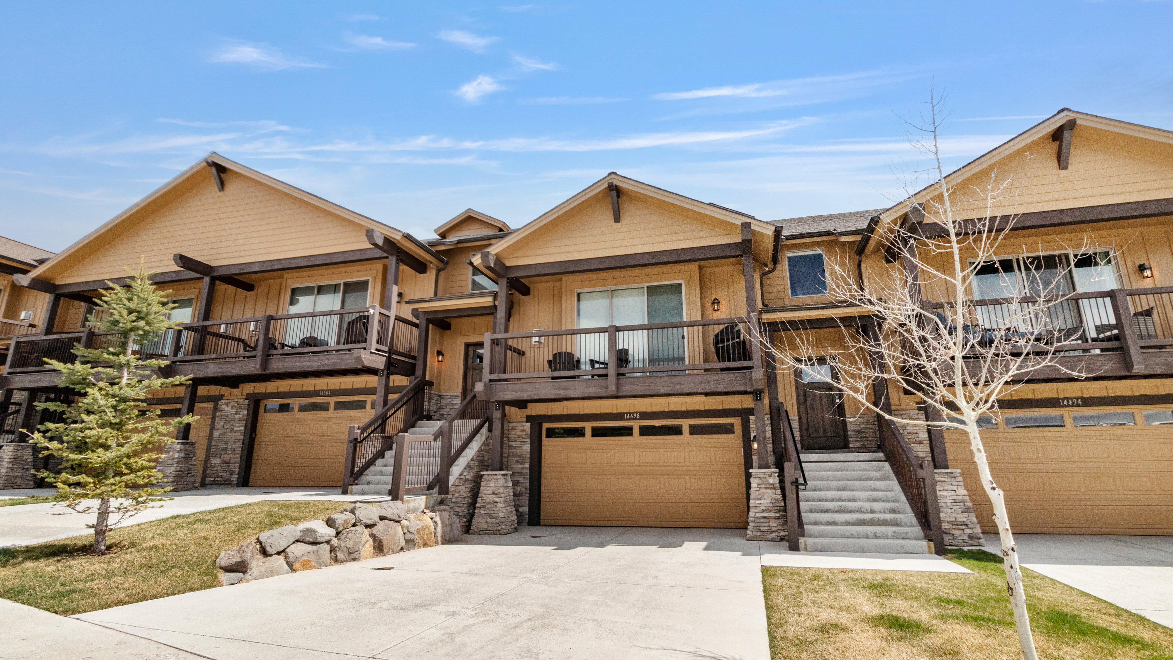 View of front of property with a garage, stone siding, driveway, board and batten siding, and a balcony