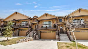 View of front of property with a garage, stone siding, driveway, board and batten siding, and a balcony