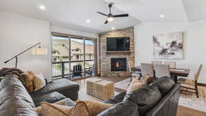 Living area with wood finished floors, a ceiling fan, a stone fireplace, vaulted ceiling, and recessed lighting