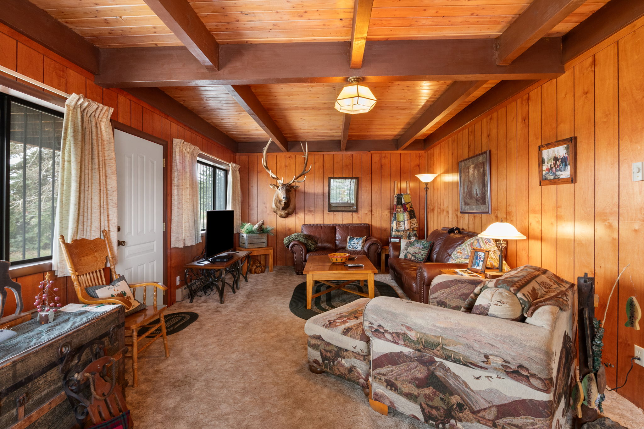 Living room featuring wood walls, carpet flooring, and a wood ceiling with exposed beams