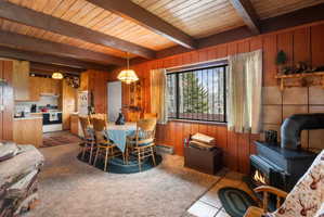 Carpeted dining room featuring a wood stove, wooden walls, a wood ceiling with exposed beams, and baseboard heating