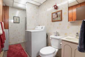 Bathroom featuring washer / dryer, vanity, a shower stall, and wallpapered walls