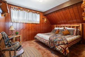 Carpeted bedroom with wood walls and vaulted ceiling