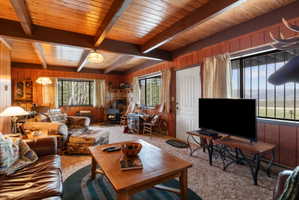 Carpeted living room featuring wooden walls and a wood ceiling with exposed beams