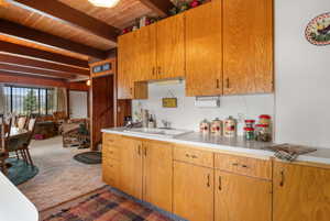 Kitchen with light countertops, carpet flooring, wood finish cabinets, a wood ceiling with exposed beams, and wooden walls