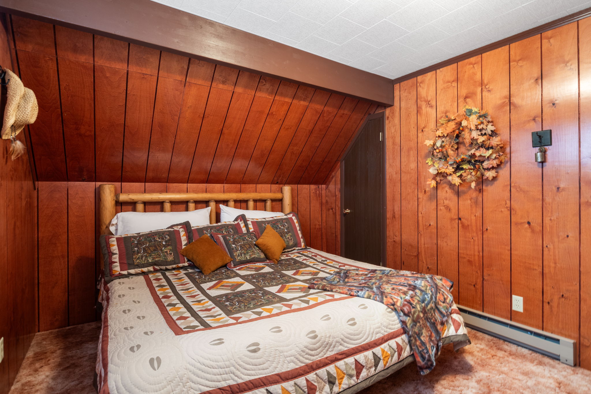 Bedroom with wooden walls, a baseboard heating unit, lofted ceiling with beams, and carpet