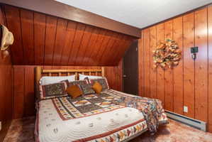 Bedroom with wooden walls, a baseboard heating unit, lofted ceiling with beams, and carpet