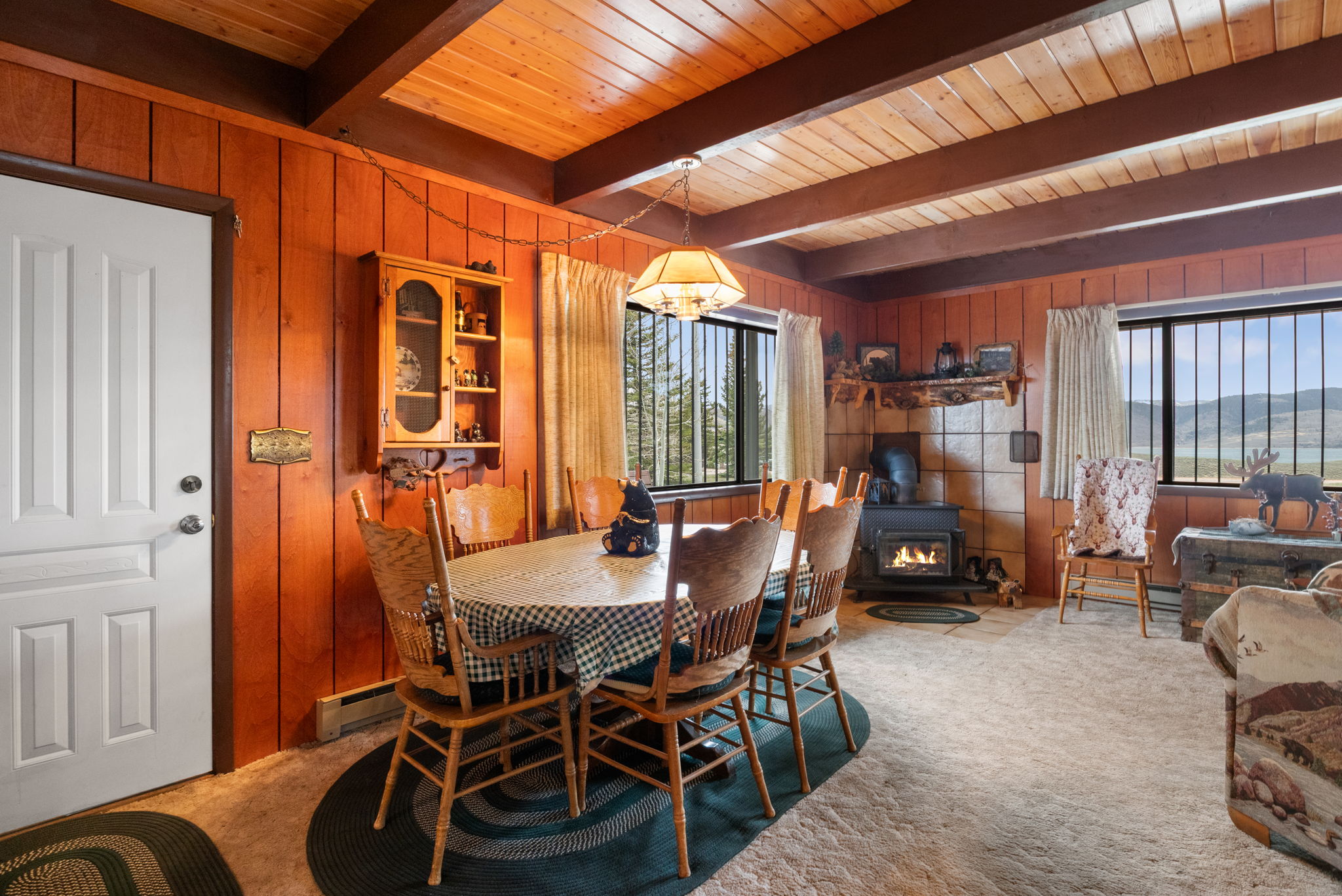 Carpeted dining space with wood walls, a wood stove, a wooden ceiling with exposed beams, and a baseboard radiator
