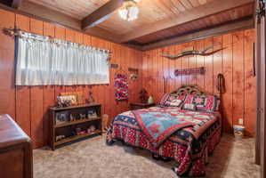 Carpeted bedroom featuring wooden walls and a wooden ceiling with exposed beams