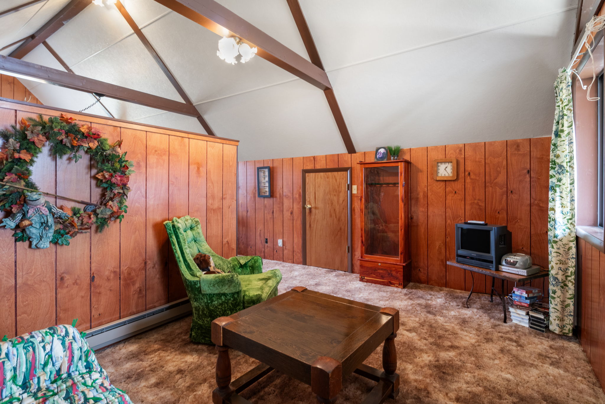 Living room with a baseboard radiator, wooden walls, dark carpet, lofted ceiling, and a chandelier