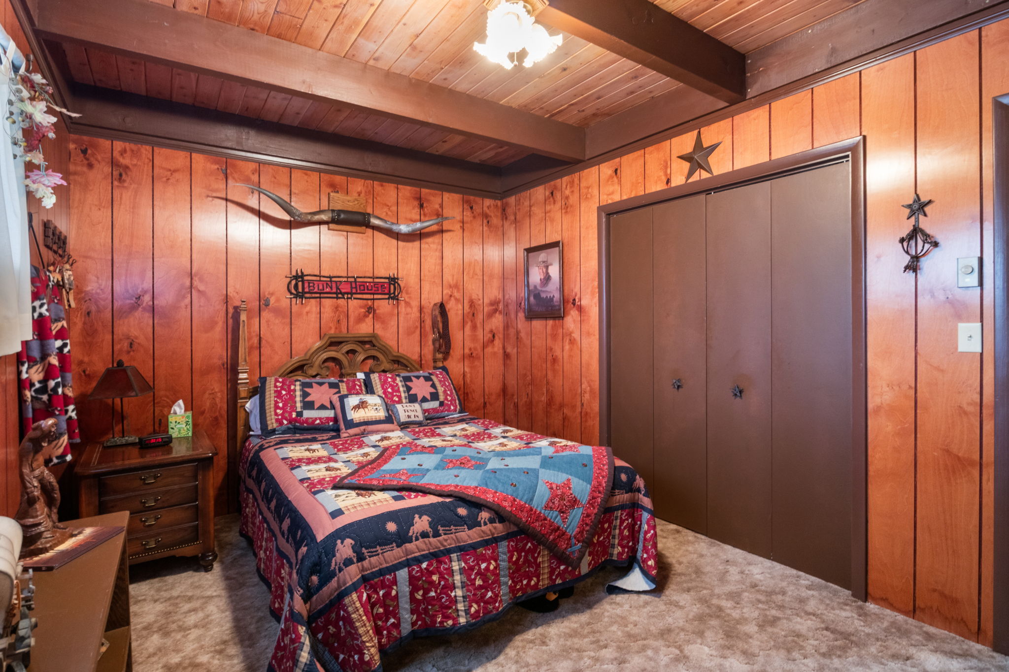 Carpeted bedroom with wood walls, a closet, and a wooden ceiling with exposed beams