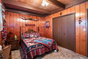 Carpeted bedroom with wood walls, a closet, and a wooden ceiling with exposed beams