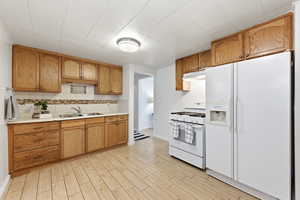 Kitchen with white appliances, light countertops, wood tiled floors, decorative backsplash, and wood finish cabinetry
