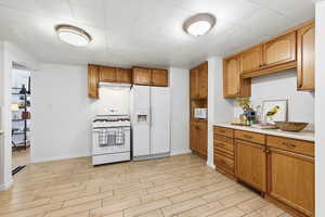 Kitchen with wood finish floors, wood finish cabinetry, white appliances, and light countertops