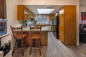 Kitchen with wood finish cabinets, light countertops, a kitchen breakfast bar, and freestanding refrigerator