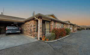 Property exterior at dusk featuring brick siding, a carport, and driveway
