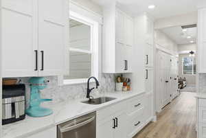Kitchen with dishwasher, white cabinetry, backsplash, light stone countertops, and recessed lighting