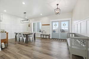 Dining area with a decorative wall, a chandelier, dark wood-style floors, and french doors