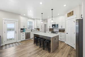 Two tone kitchen featuring stainless steel appliances, a kitchen breakfast bar, a center island, dual tone cabinets, and decorative light fixtures