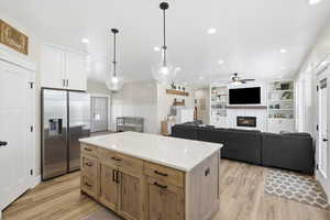Kitchen with a kitchen island, stainless steel fridge with ice dispenser, open floor plan, light stone counters, and a glass covered fireplace