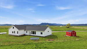 Back of property with a shed, a rural view, a mountain view, and a lawn