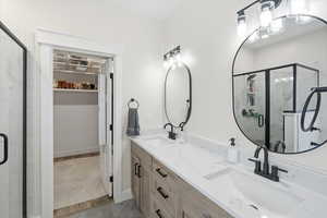 Bathroom featuring a marble finish shower, double vanity, and a spacious closet