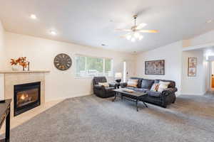 Open living area with a tile fireplace, ceiling fan, carpet, and vaulted ceiling