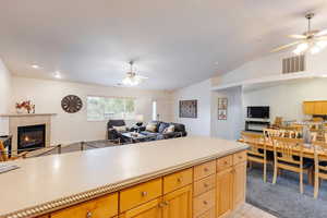 Kitchen with open floor plan, ceiling fan, light soap countertops, a tile fireplace, and lofted ceiling