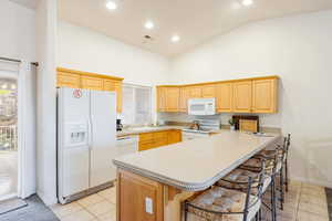 Kitchen with light wood finish cabinets, white appliances, solid stone  countertops.