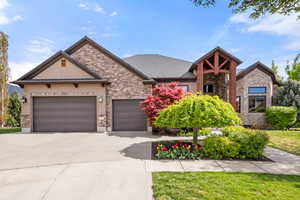View of front facade with stone siding, an attached garage, concrete driveway, stucco siding, and a front yard