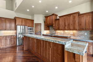 Kitchen with wood finish cabinetry, stainless steel appliances, a large island with sink, dark wood-style floors, and recessed lighting
