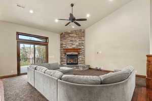 Living area with lofted ceiling, a stone fireplace, a ceiling fan, dark wood-type flooring, and dark colored carpet