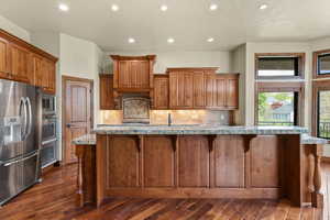 Kitchen with stainless steel appliances, wood finish cabinetry, recessed lighting, a breakfast bar, and light stone counters