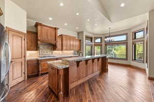 Kitchen featuring wood finish cabinetry, a kitchen island with sink, stainless steel appliances, hanging lights, and decorative backsplash