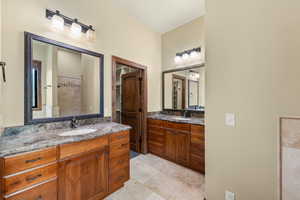 Bathroom with two vanities, tiled shower, and light tile patterned floors
