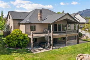 Rear view of house with a hot tub, a patio, a chimney, stucco siding, and stone siding