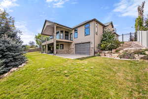 Rear view of property featuring stucco siding, a garage, a patio area, stone siding, and a balcony