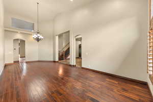 Unfurnished room featuring arched walkways, dark wood-style flooring, suspended lighting, and vaulted ceiling