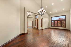 Empty room featuring dark wood-type flooring, lofted ceiling, a chandelier, and arched walkways