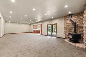 Unfurnished living room featuring light colored carpet, recessed lighting, and a wood stove