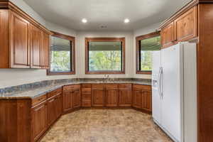 Kitchen featuring white fridge with ice dispenser, wood finish cabinetry, and recessed lighting