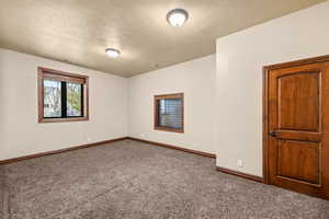 Carpeted empty room featuring a textured ceiling and baseboards