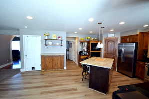 Kitchen with stainless steel appliances, light wood-type flooring, light stone countertops, a center island, and a kitchen breakfast bar