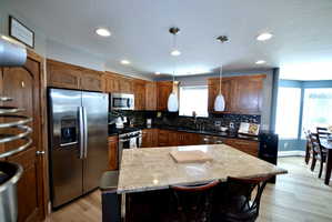 Kitchen with stainless steel appliances, a center island, a kitchen bar, pendant lighting, and light wood-style floors