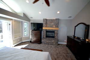 Bedroom with lofted ceiling, a ceiling fan, dark carpet, access to exterior, and a fireplace