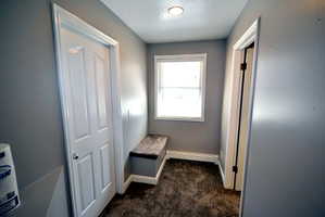 Hallway with dark carpet, a textured ceiling, and a baseboard heating unit