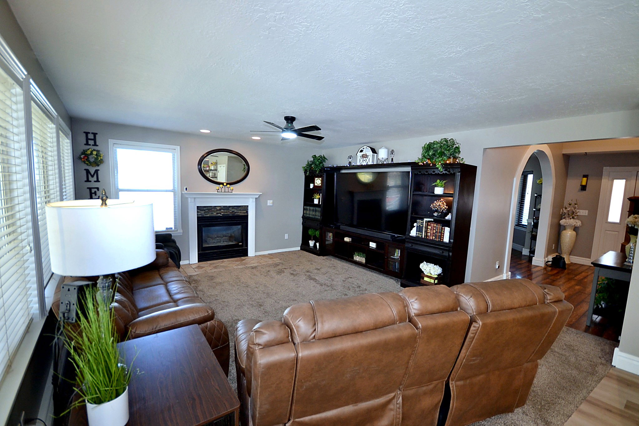 Living area featuring arched walkways, a premium fireplace, a ceiling fan, a textured ceiling, and wood finished floors